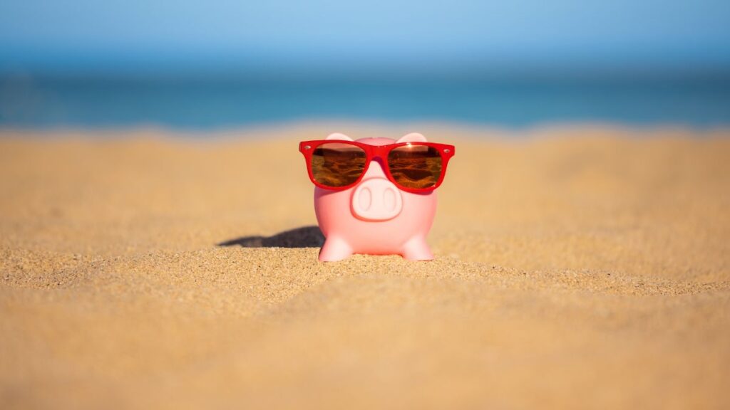 A piggy bank at the beach wearing sunglasses