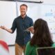 Male teacher smiling in front of the class students and explaining