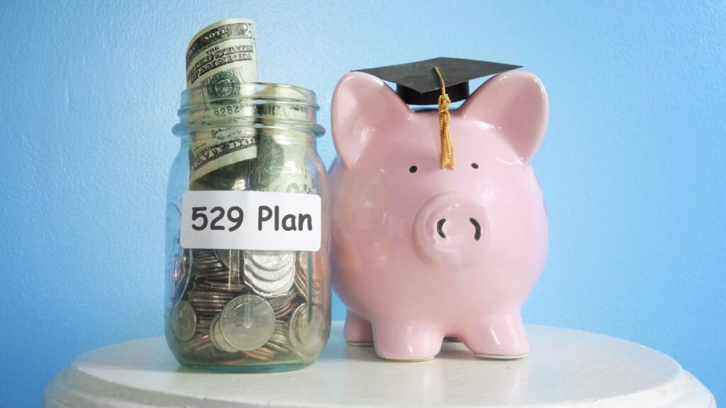A pink piggy bank wearing a graduation cap next to a money jar with 529 plan text on it