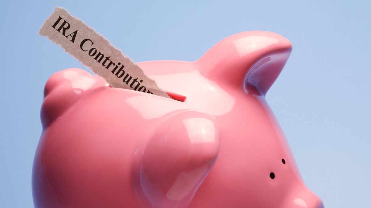 A slip of paper that says IRA contribution being inserted into a pink piggy bank